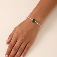 Garbo oval emerald tennis bracelet with gold setting and clear stones on wrist