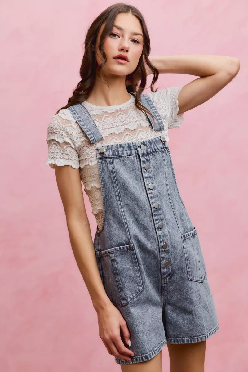Light wash denim overall romper with adjustable straps, button front, and patch pockets