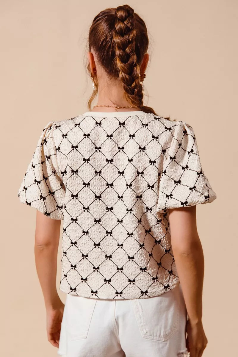 Ivory woven bubble sleeve top with black bow texture pattern, back view