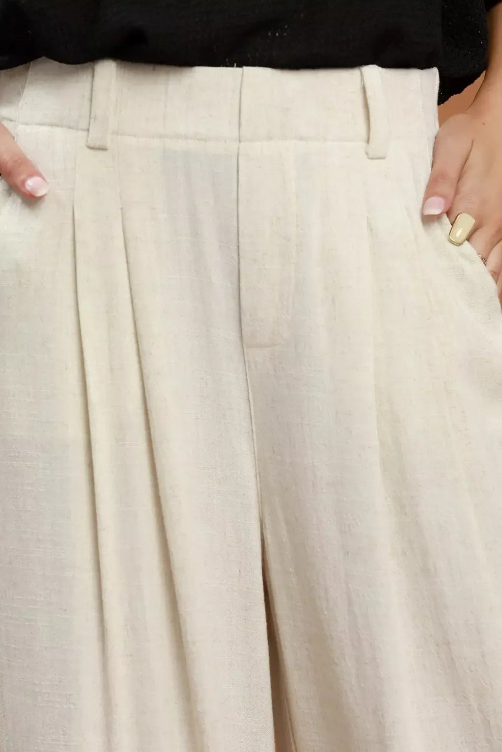 Cream trousers close-up: pleated front, waistband, and belt loops