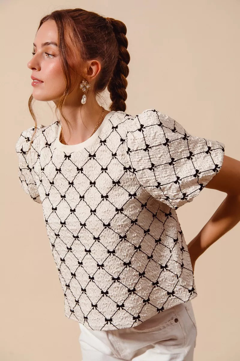 Ivory woven bubble sleeve top with black bow texture pattern, side view