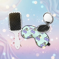 Set of hairbrush, compact mirror, and cherry-themed eye mask on a pastel background