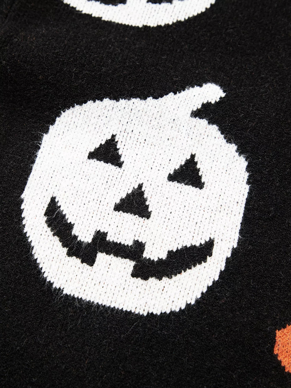 Black sweater close-up of large white jack-o-lantern face motif with orange accents