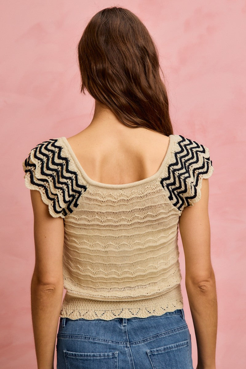 Back of oatmeal knit top with wavy texture and black zigzag flutter sleeves