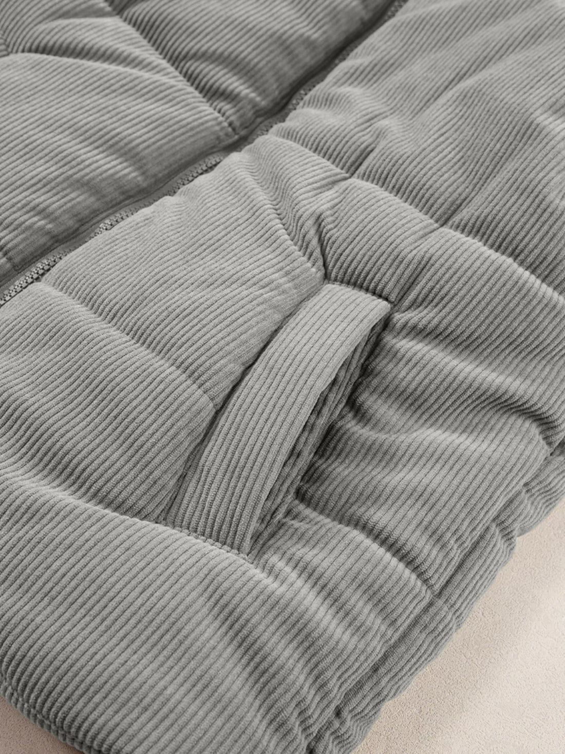 Gray corduroy puffer vest side close-up showing quilted baffles and seam stitching.