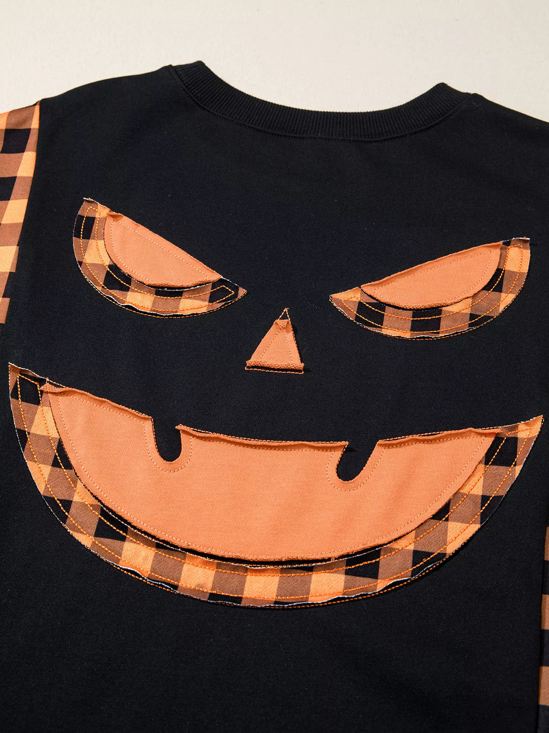Close-up of black top with orange plaid pumpkin face applique on chest