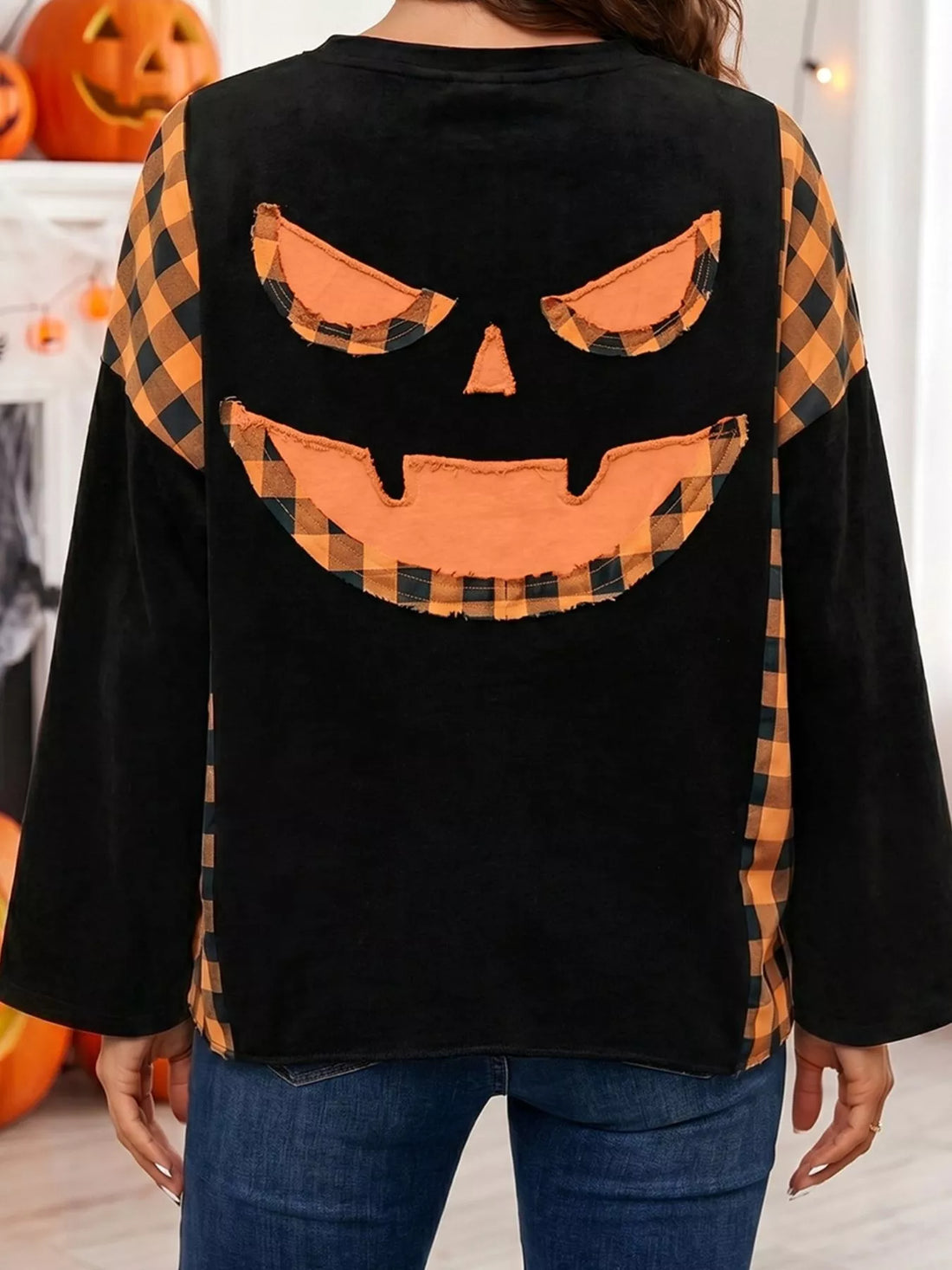 Black long-sleeve top back view featuring orange plaid pumpkin face applique