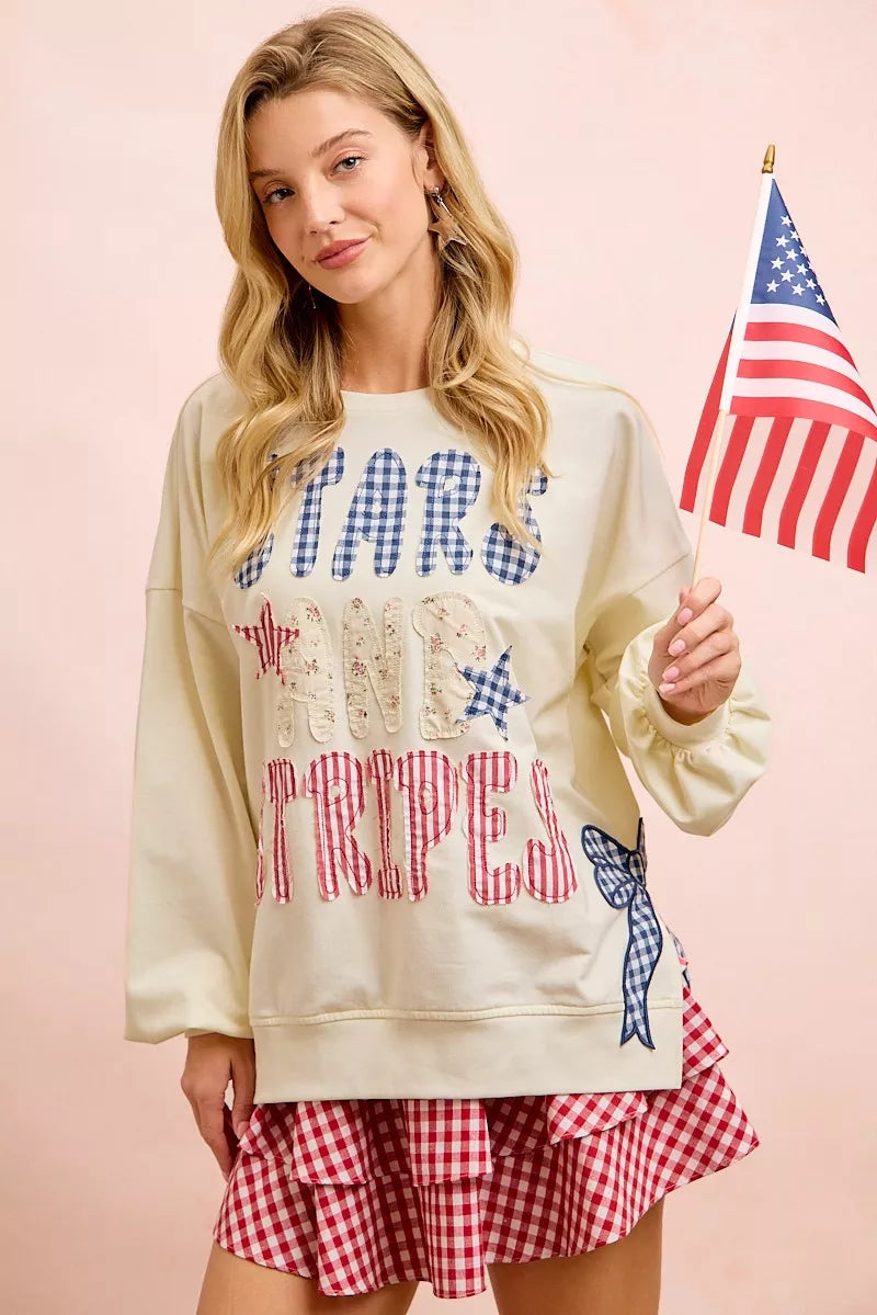 Cream sweatshirt with blue star top, red stripe bottom, and blue bow patch at hem.