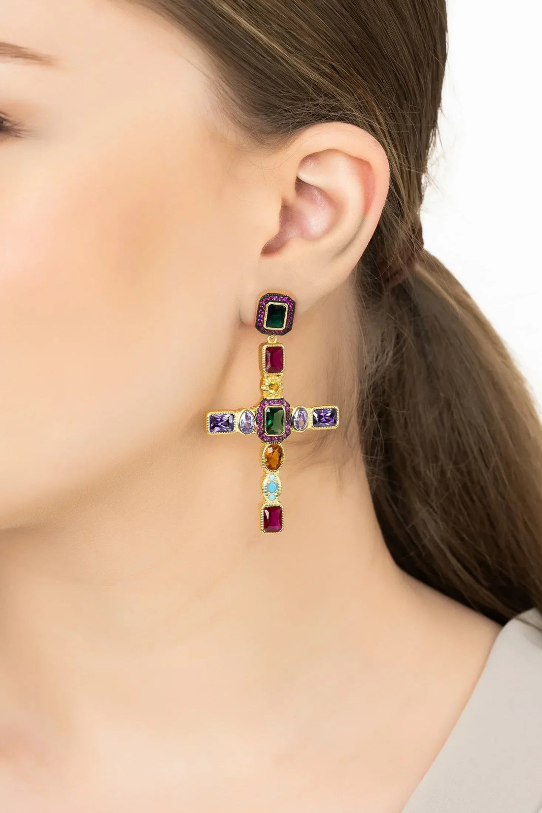 Gold cross gemstone earrings with multicolor stones, worn on ear
