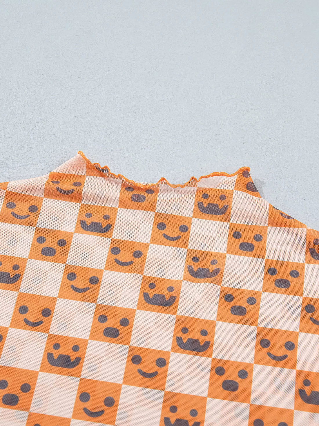 Close-up of orange-and-white checker pattern with jack-o’-lantern faces on lightweight blouse fabric