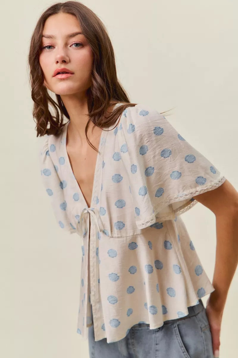 Ivory blouse with blue dot print, V-neck tie front, and layered flutter sleeves.