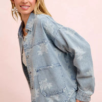 Light blue denim jacket with white floral print, chest flap pocket and rolled sleeve cuff