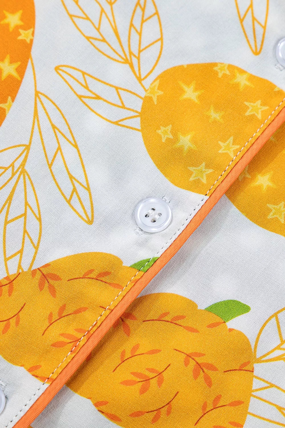 Button placket detail with orange piping and pumpkin print on white fabric