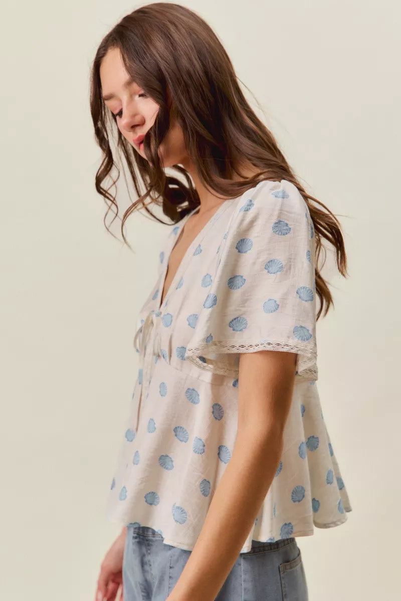 Ivory blouse with blue dot print, tie-front V-neck, and flutter sleeves.