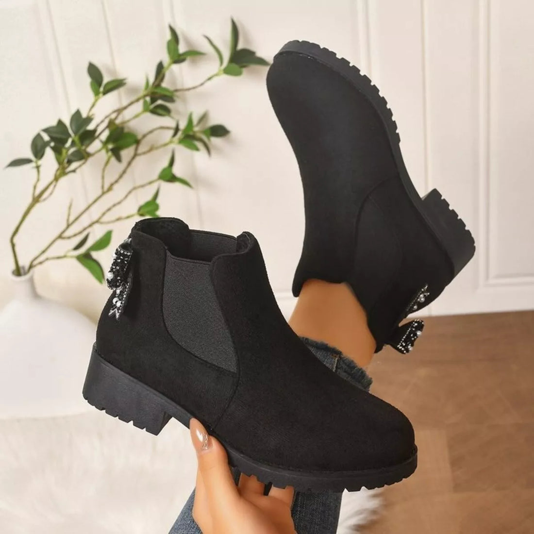 Black suede ankle boots with round toe, block heel, and jeweled bow side detail