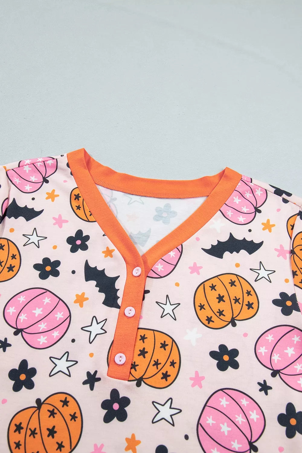 Close-up: dusty pink pumpkin-print long-sleeve top with orange V-neck button placket