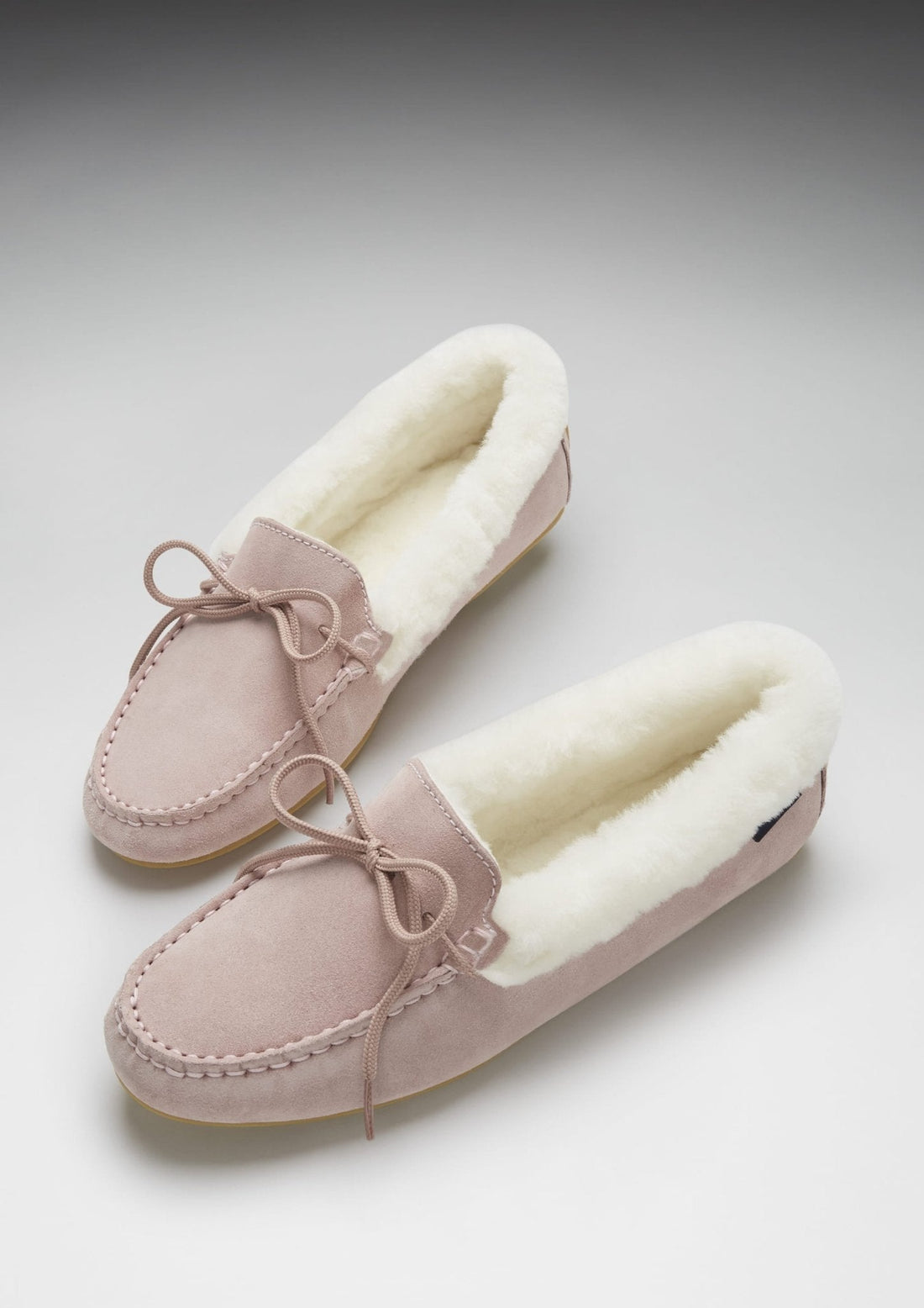 Pair of pink suede sheepskin slippers with fleece lining and bow ties