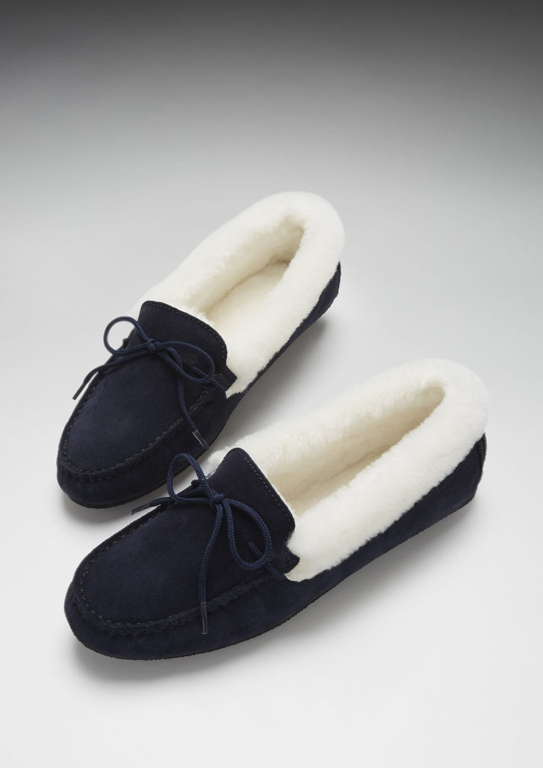 Pair of navy suede slippers with plush cream sheepskin linings and bow ties