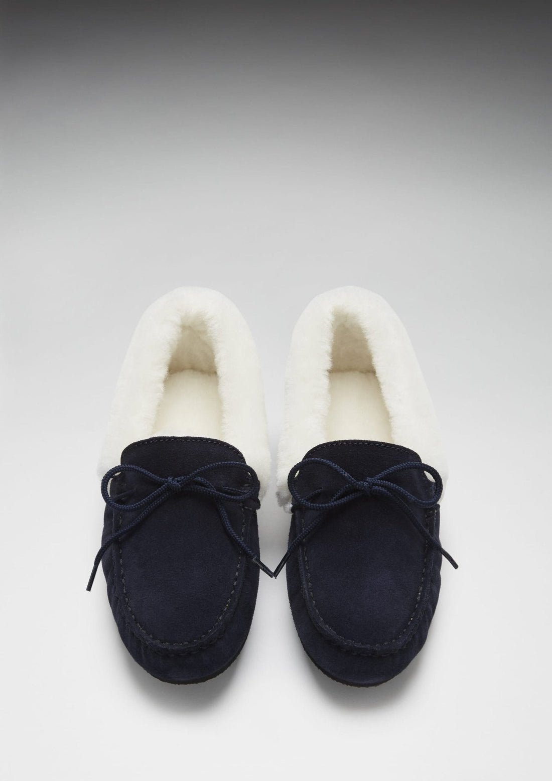 Top view of navy suede slippers with moccasin stitching and cream linings