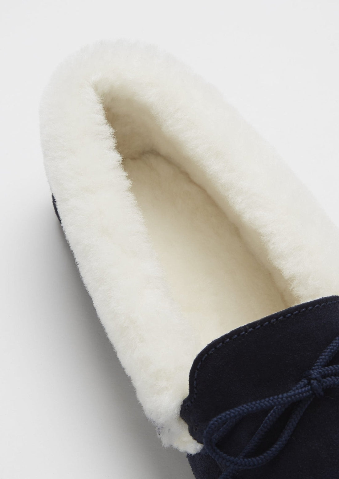 Close-up of the cream sheepskin lining inside a navy suede slipper