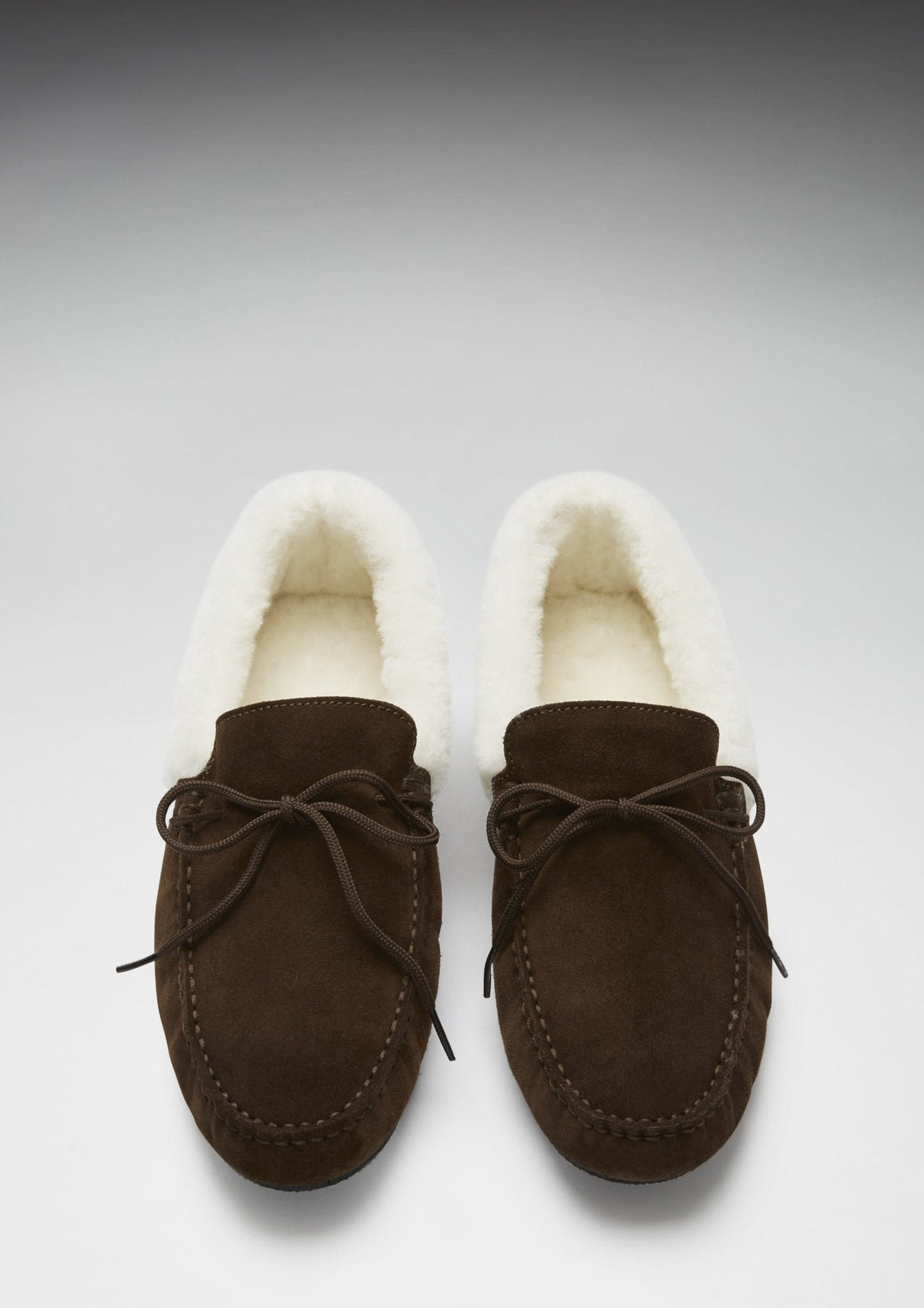 Pair of brown suede slippers shown from above, with cream lining and lace-up fronts