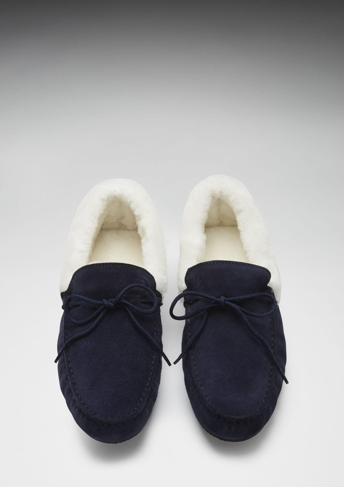 Pair of navy suede slippers shown from above, with cream sheepskin lining