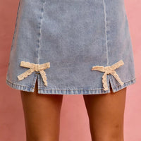 Light blue denim mini skirt with lace ribbon bow trim at the front hem.
