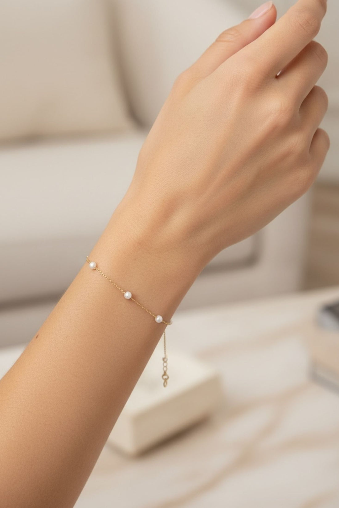 Gold pearl bracelet on wrist with small round white pearls and chain links