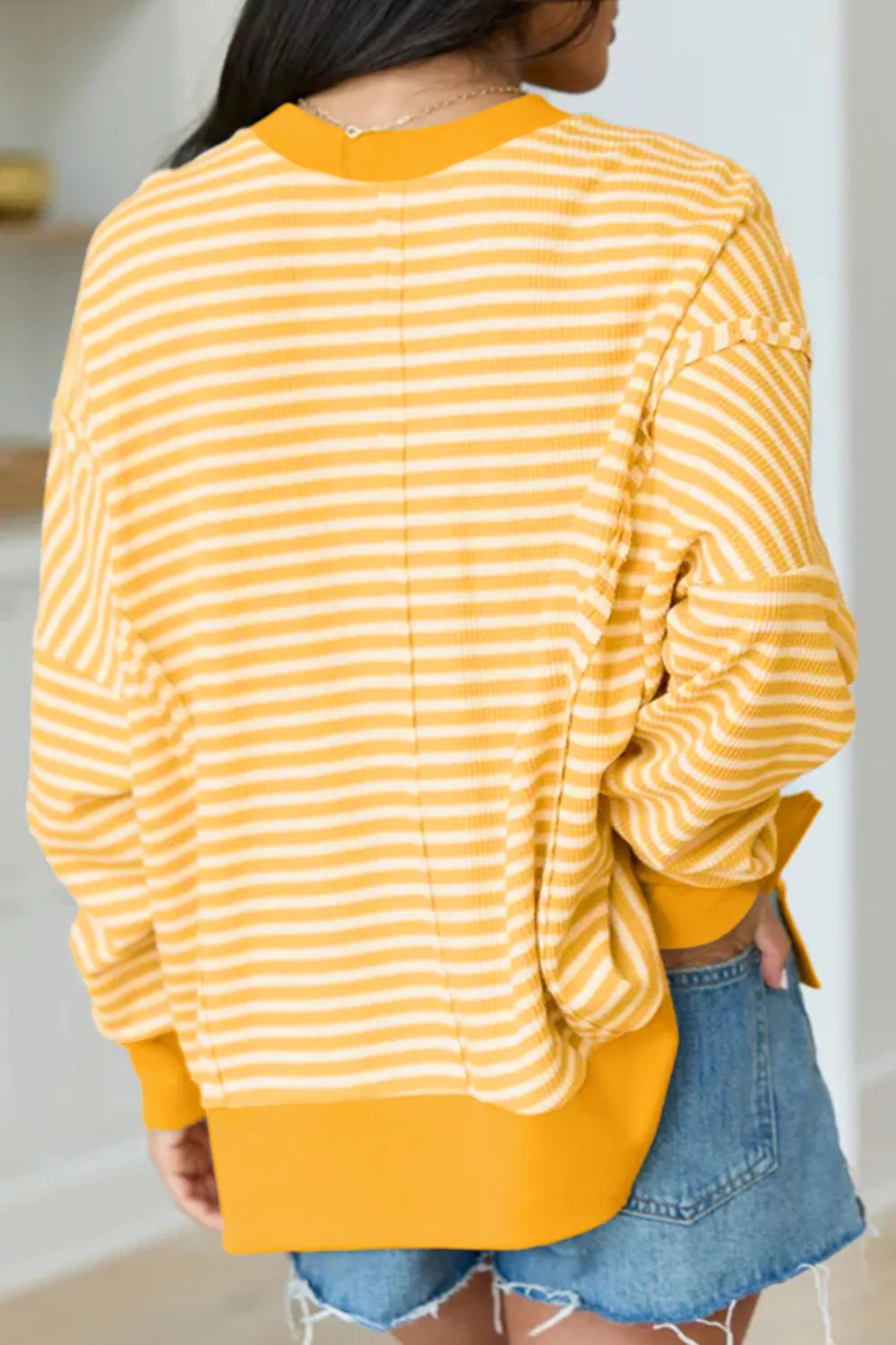 Back view of gold-and-white striped long-sleeve top with orange split-hem detail