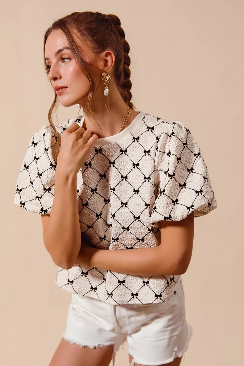 Ivory woven bubble sleeve top with black bow texture pattern, front shoulder detail