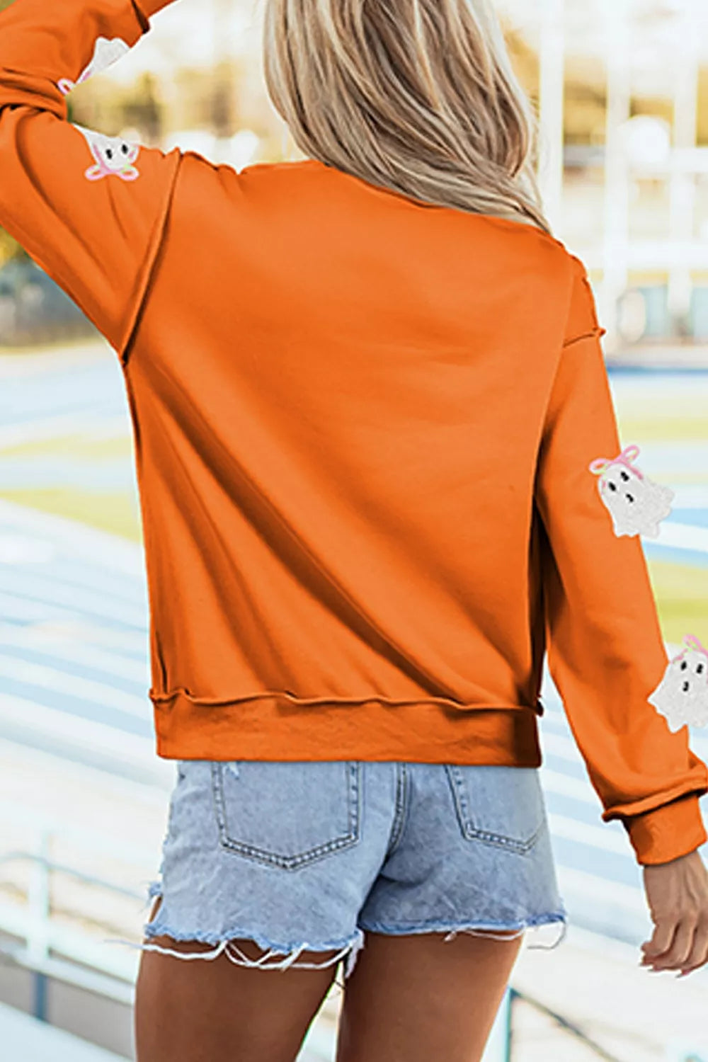 Orange mock neck sweatshirt, back view, ghost appliques and ribbed hem