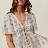 Ivory dot-print tie-front blouse with flutter sleeves and V-neck trim.