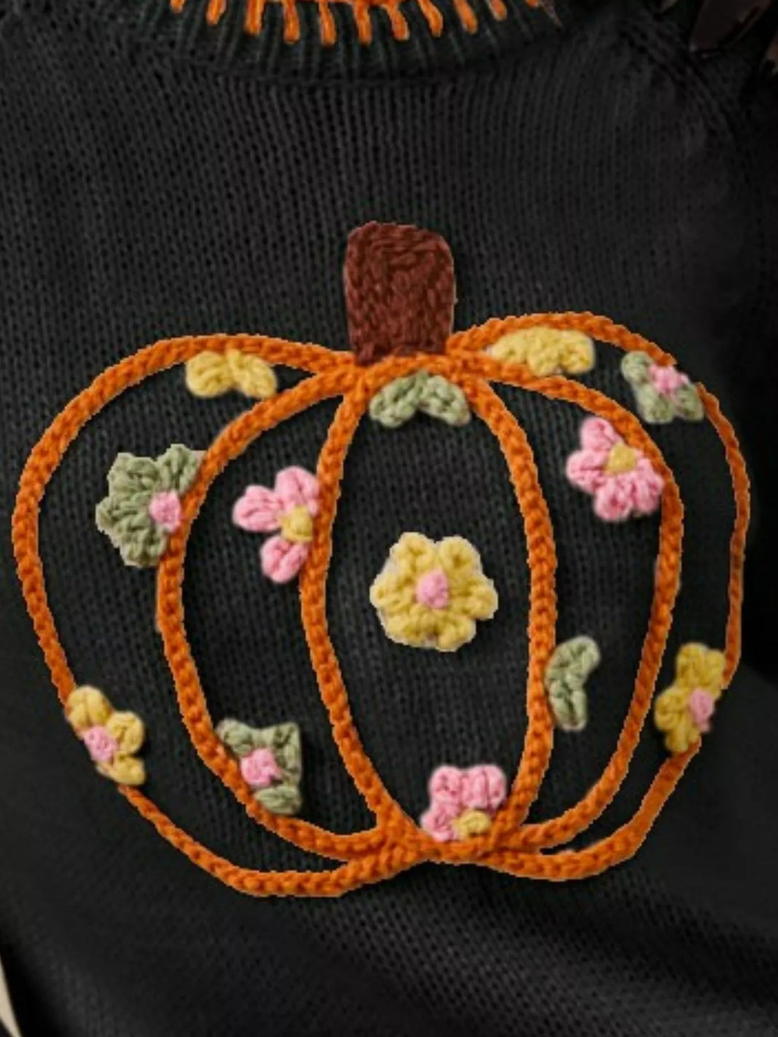 Black knit sweater close-up: orange stitched pumpkin with colorful flower embroidery