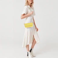 Yellow mini leather shoulder bag worn with front flap and gold chain strap.