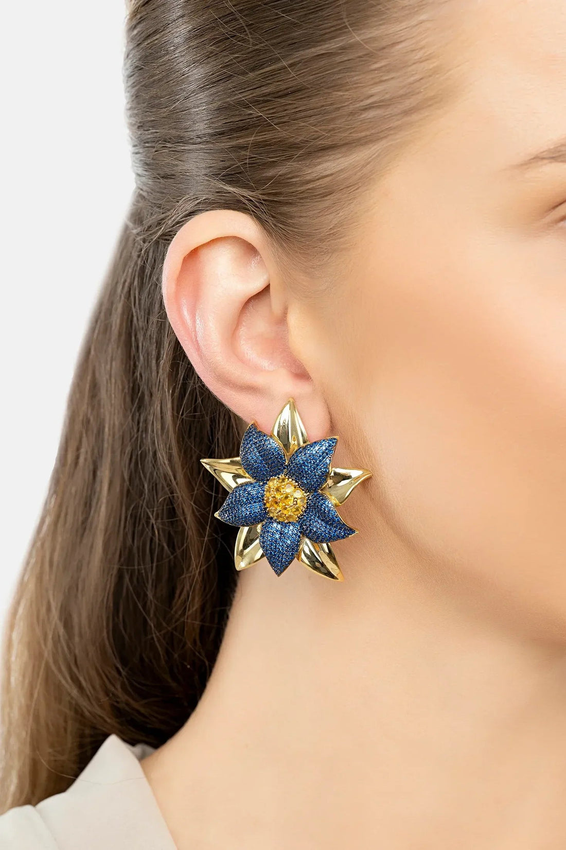 Close-up of blue daisy flower stud earrings with gold-tone details and textured center.