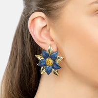 Close-up of blue daisy flower stud earrings with gold-tone details and textured center.