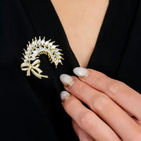 Gold ribbon and laurel leaf brooch with crystal-like stones on black clothing