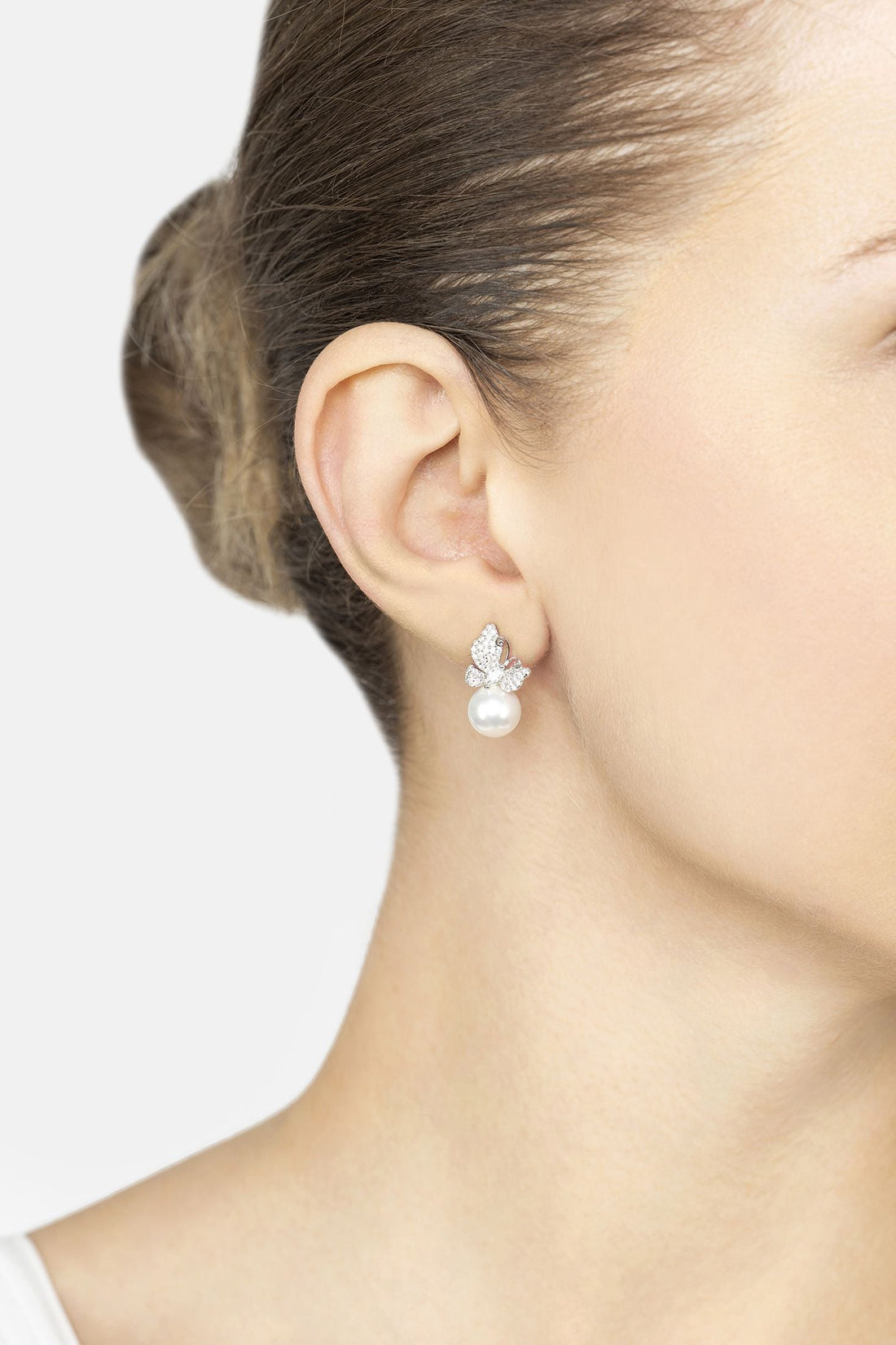 Butterfly stud-and-drop earrings with pearl drops on a model’s ear