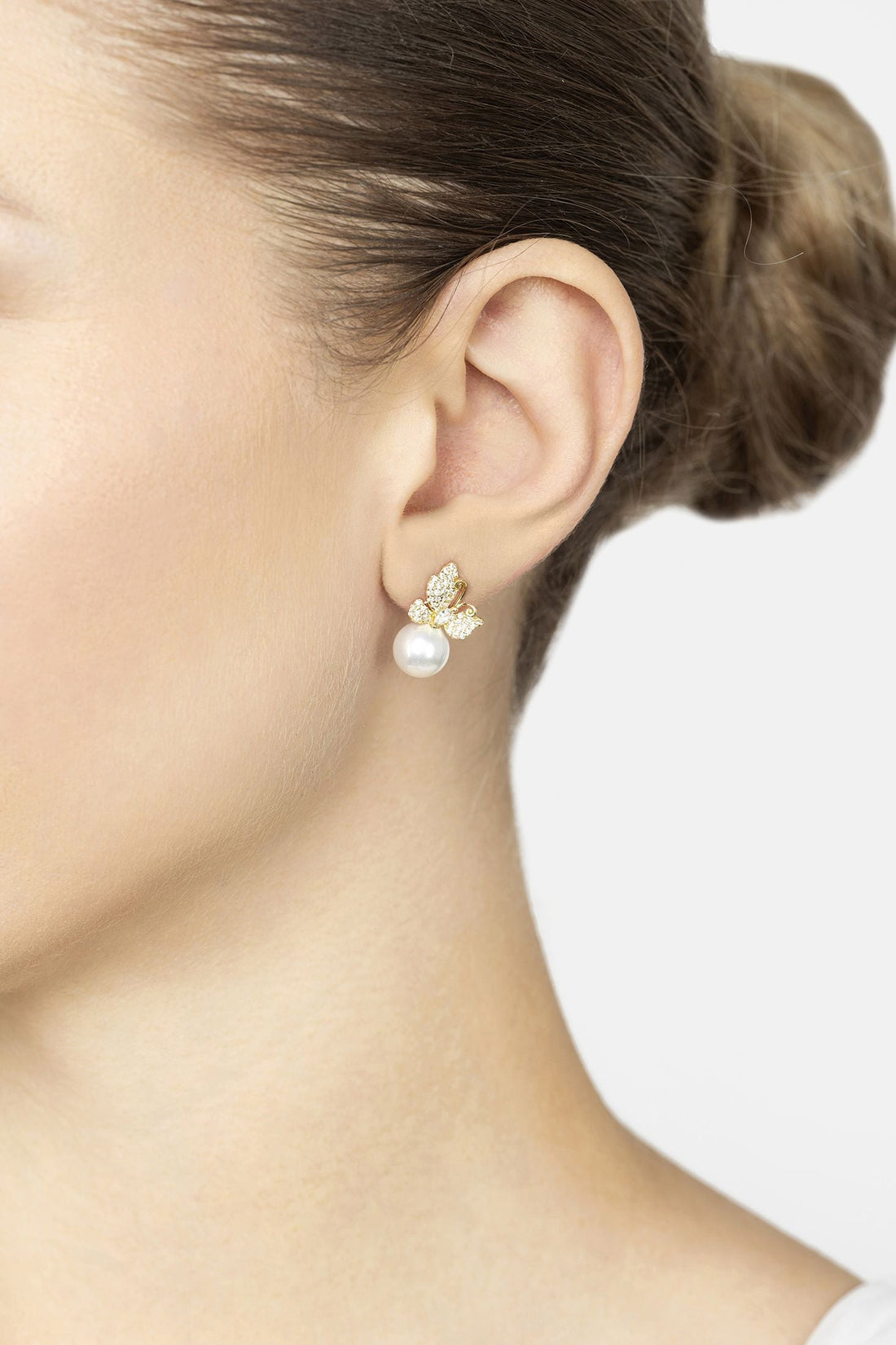 Gold butterfly drop earrings with rhinestone wings and white pearl on earlobe