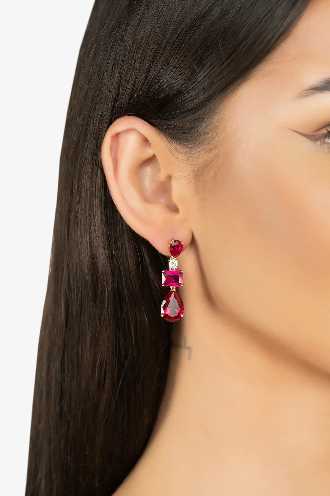 Gold drop earrings with ruby-red stones, worn on model with dark hair side view