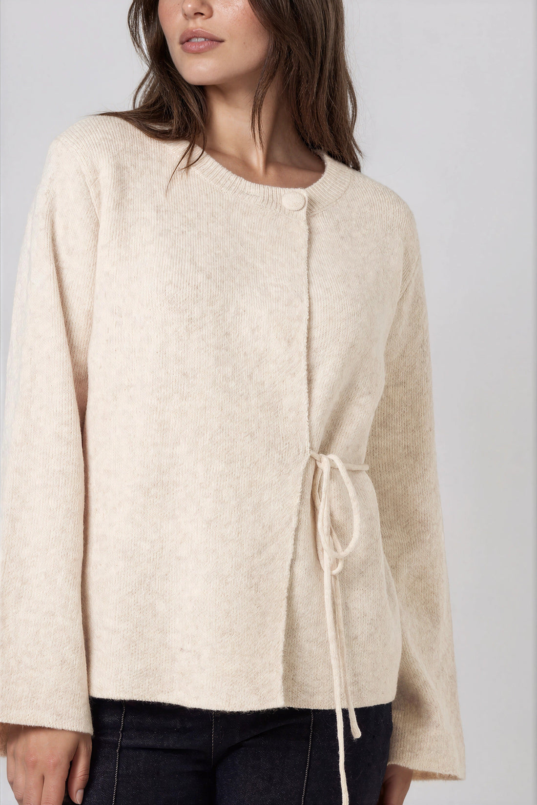 Beige knit cardigan with round neck and adjustable side ties; wide sleeves