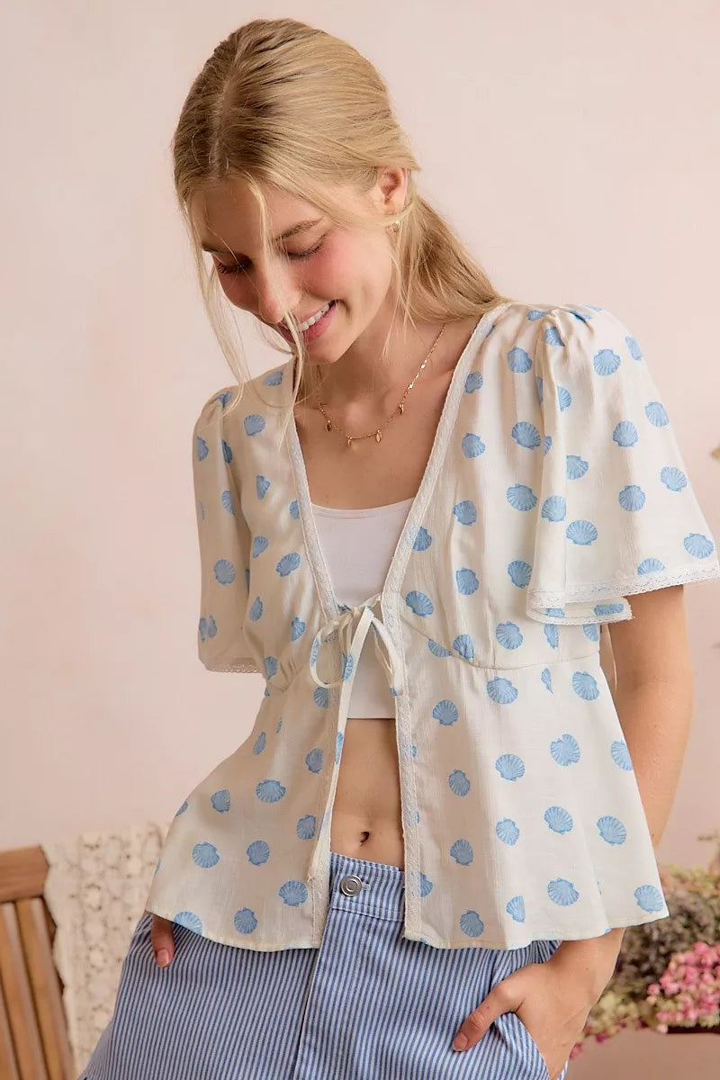Ivory dot-print blouse with V-neck tie front and puffed flutter sleeves.
