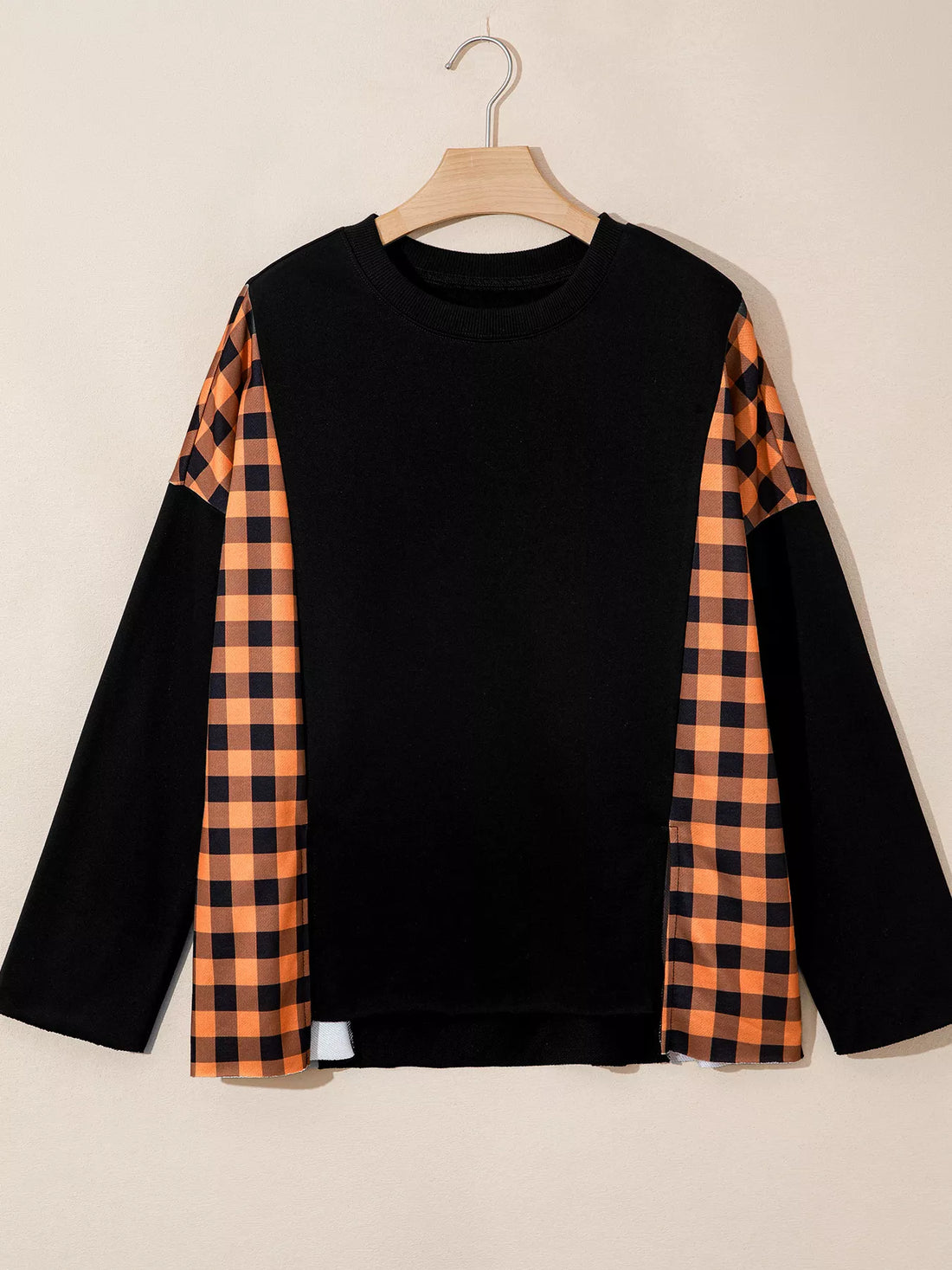 Black long-sleeve top on hanger with orange plaid sleeve panels