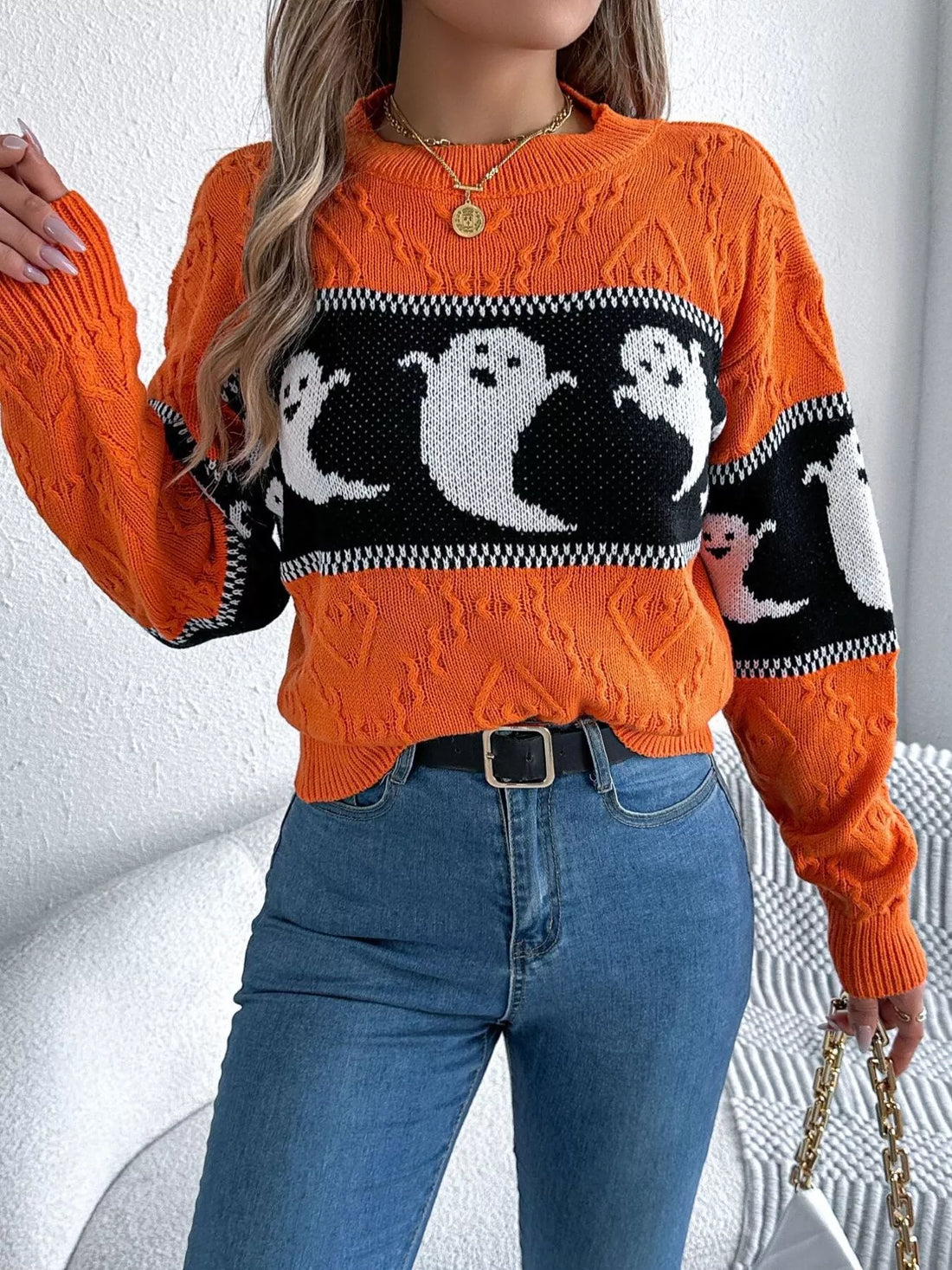 Orange textured crewneck sweater with black-and-white ghost motif and ribbed wrist cuffs