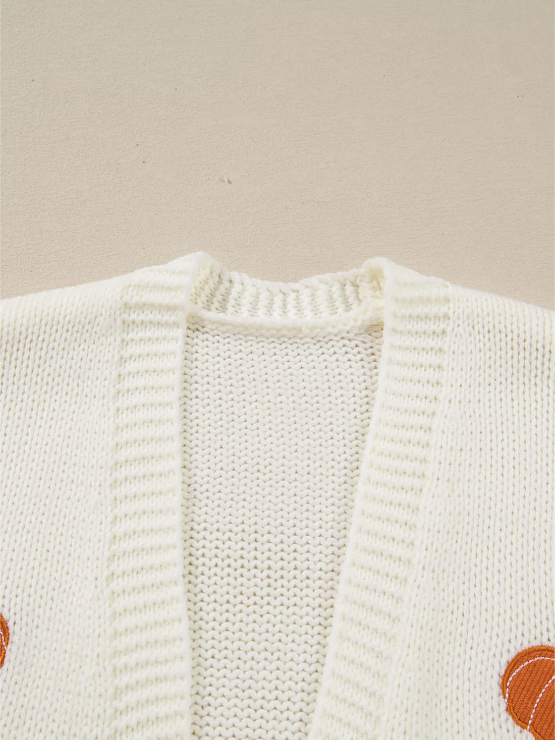 Close-up of off-white knit cardigan with open front and pumpkin embroidery patch.