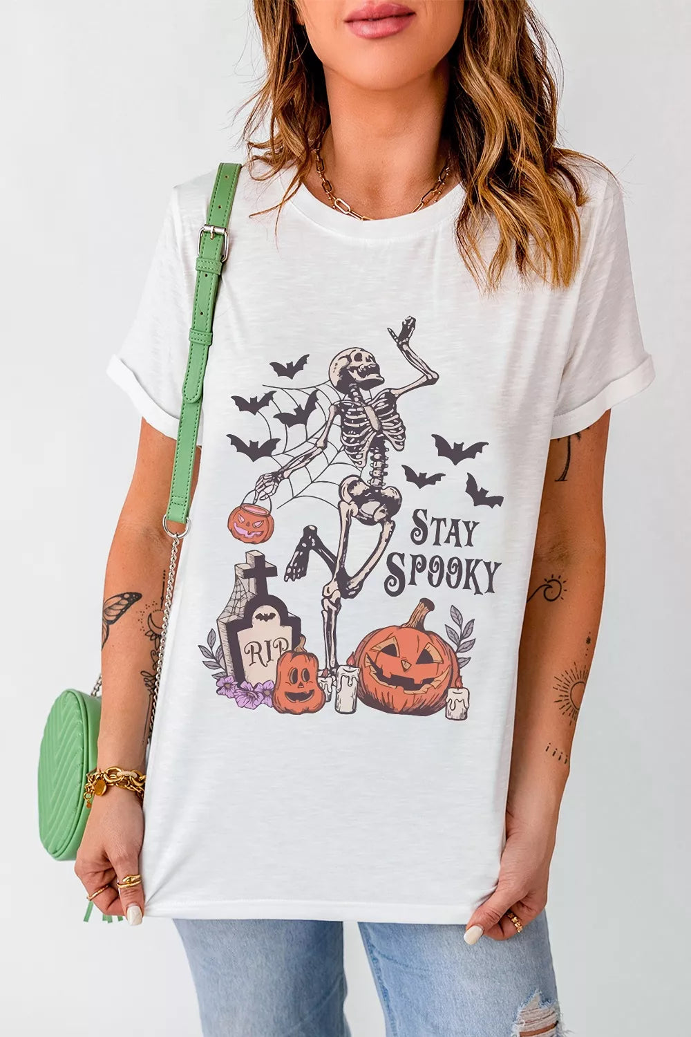 White Halloween graphic T-shirt front: skeleton with bats, pumpkins, and &