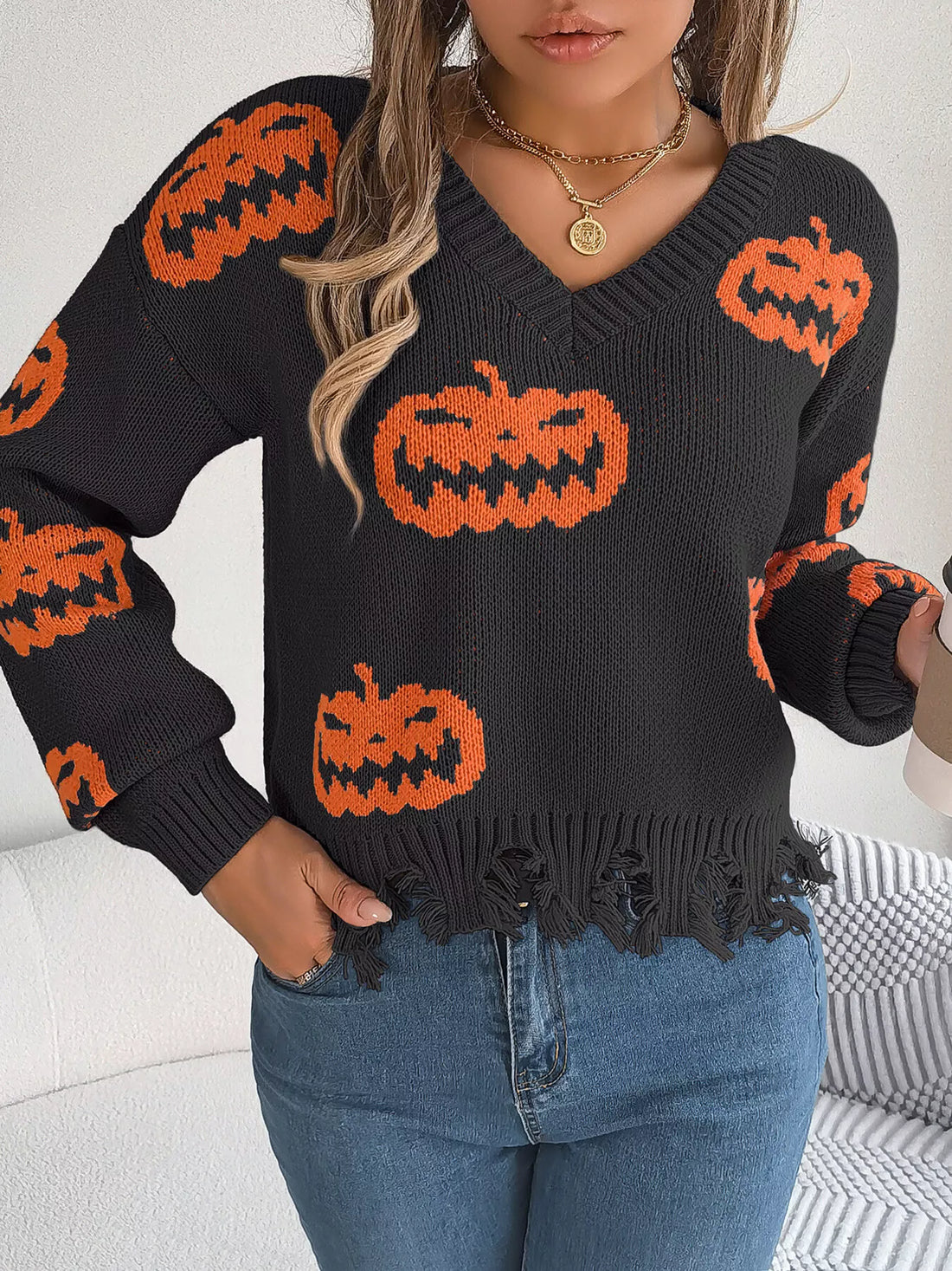 Black knit V-neck sweater with orange jack-o’-lantern motifs and distressed frayed hemline