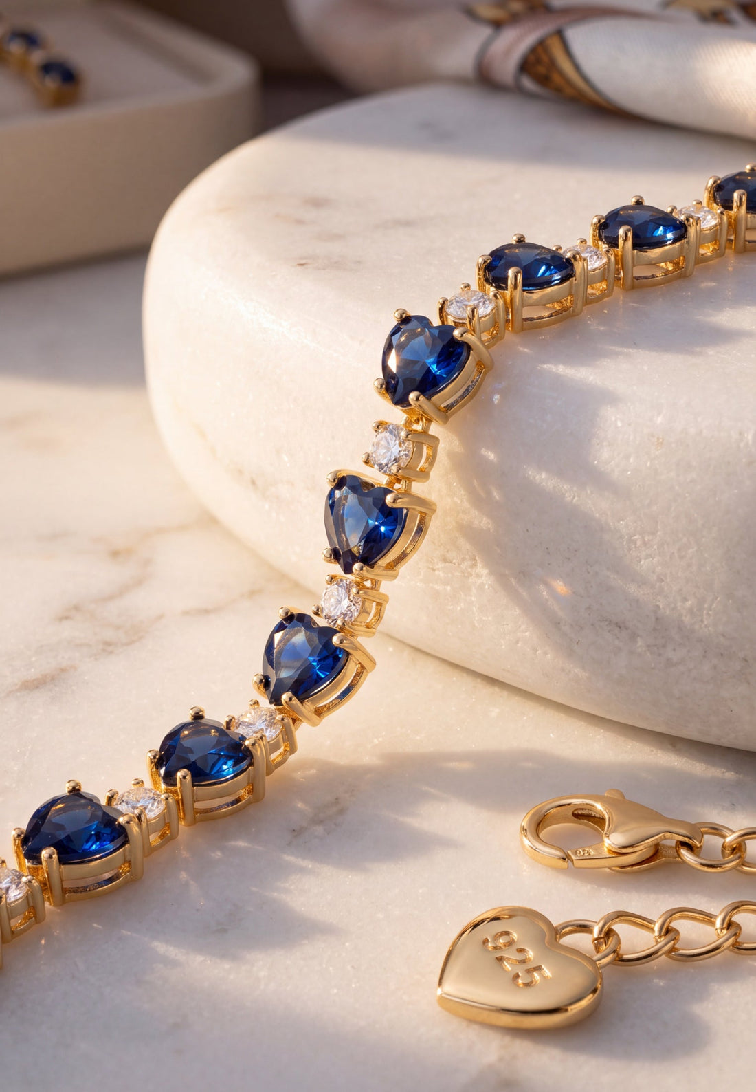 Gold-tone tennis bracelet close-up with blue faceted stones and heart charms