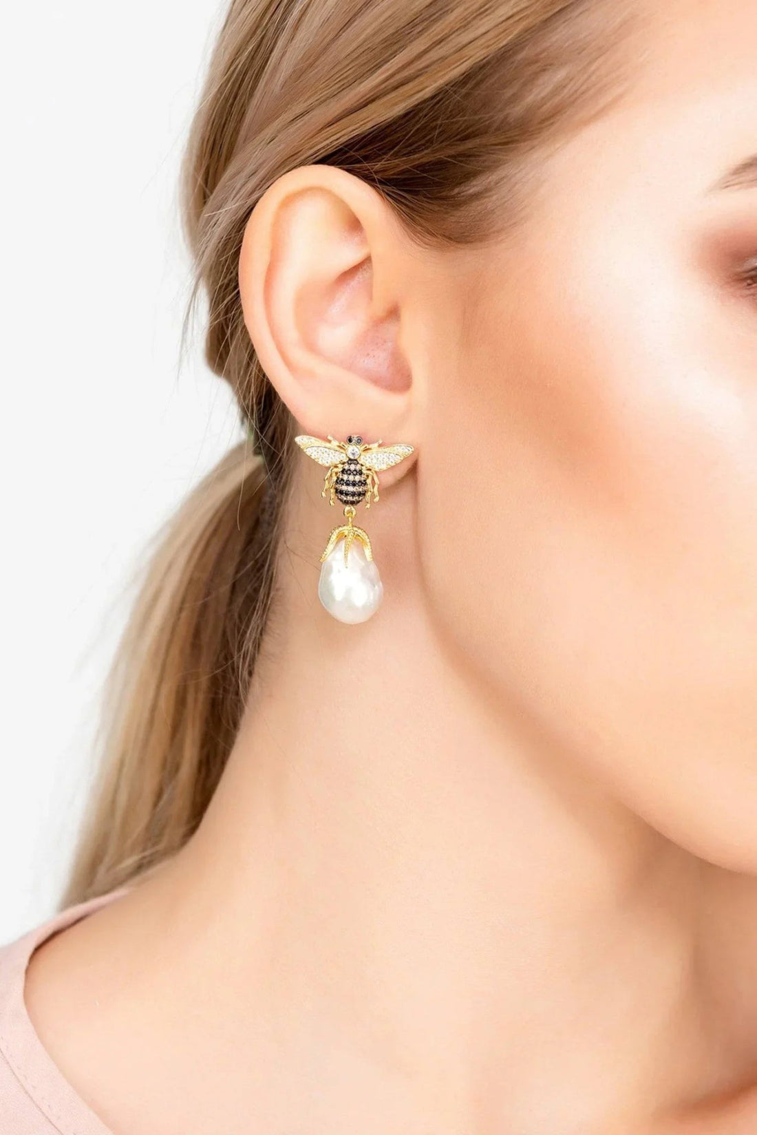 Gold-tone bee earrings with crystal wings and white pearl drop, worn on ear
