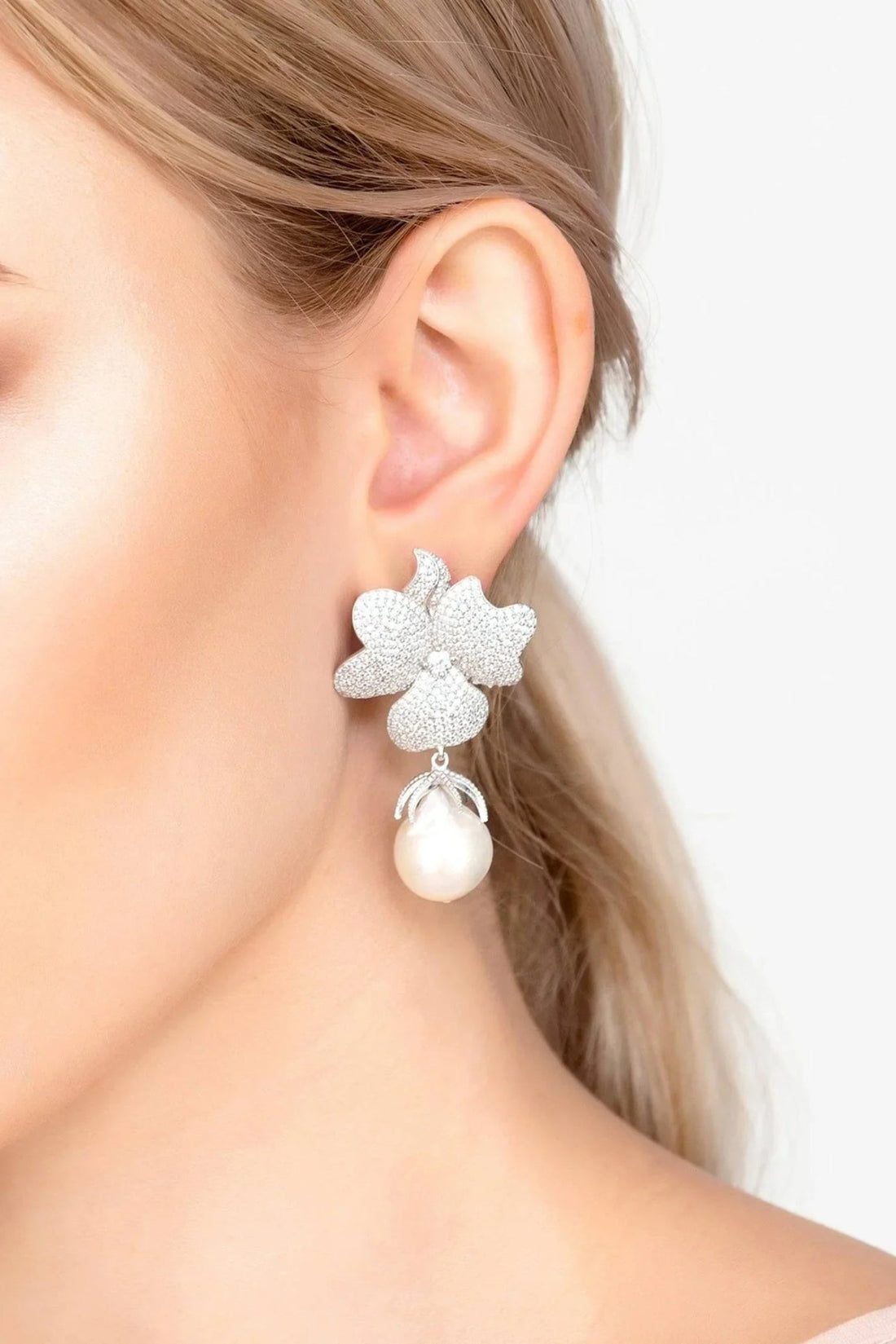 Silver textured flower drop earrings with white pearl, shown on ear